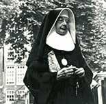 A nun wearing traditional attire, holding a small object in her hands.