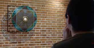A person observing a circular stained glass piece on a brick wall.