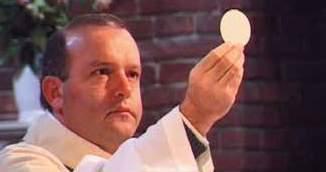 A priest holding a large Communion host during a religious ceremony.