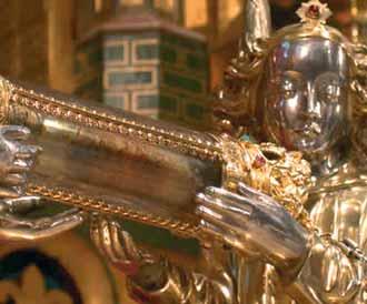 A silver figure holding a cylindrical relic, adorned with gold and jewels.