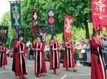 A procession featuring participants in red robes carrying banners and walking through a street.