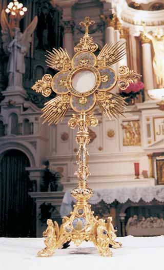 An ornate monstrance displayed in a church setting, featuring intricate gold detailing and religious symbols.