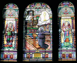 A stained-glass window showing a kneeling figure in prayer, surrounded by ornate designs and religious symbols.