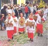 Children in ceremonial attire participating in a religious procession, carrying decorative items.