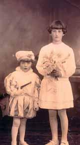 Two children dressed in traditional attire, one holding a bouquet of flowers.