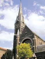 A tall church with a spire surrounded by trees and a blue sky.