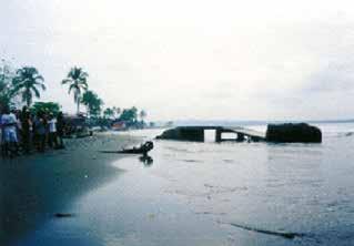 A beach scene showing a group of people near a damaged structure by the water.