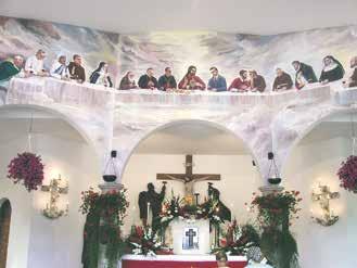 Interior view of a church with a mural depicting the Last Supper and floral decorations.