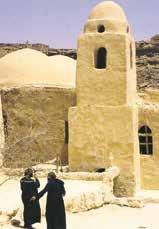 Two monks stand in front of a desert monastery with a dome.