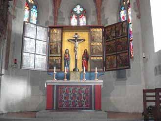 An altar with a crucifix and two statues of saints, surrounded by stained glass windows.