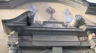 The image shows the ornate facade of a church with two figures and a central monstrance.