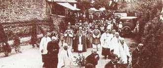 A historical procession with clergy and people in a village setting.