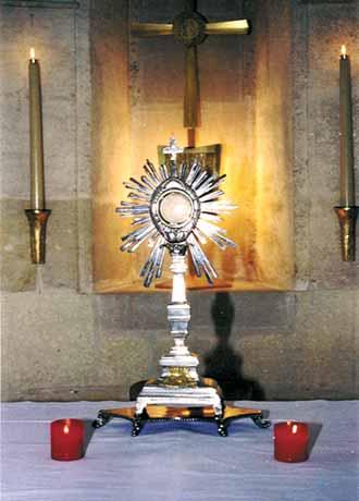 A monstrance displaying the Eucharistic host with lit candles on either side.
