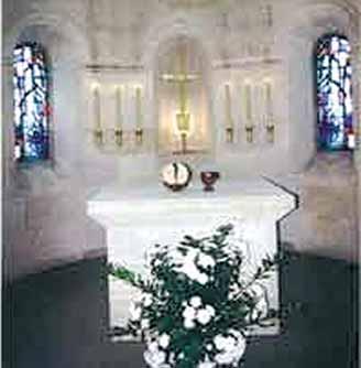 A serene altar with candles, a chalice, and a floral arrangement in a church interior.