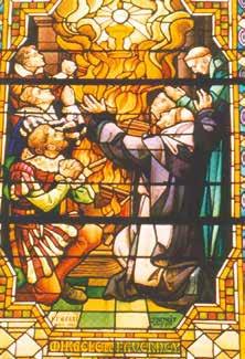 Stained glass depiction of monks and people in prayer before a burning monstrance.