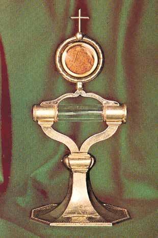 A silver monstrance holding a relic of the miraculous Host, displayed against a green background.