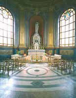An ornate church interior with large windows, an altar, and rows of chairs.