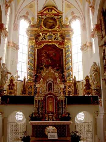 An ornate altar with statues and stained glass windows in a church interior.
