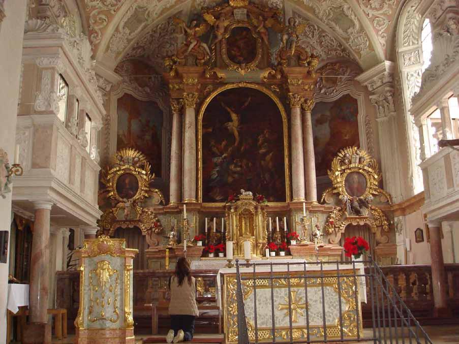 Interior view of a church altar with ornate decorations and a person kneeling in prayer.