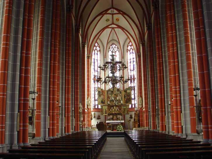 Interior view of a church featuring tall red columns and a prominent altar.