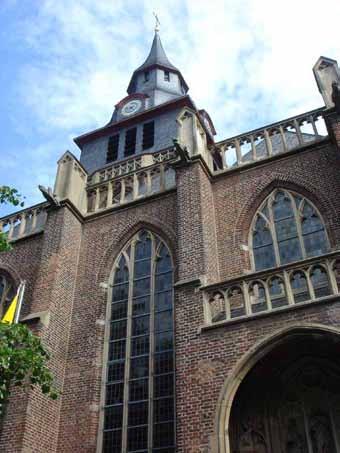 The image shows the exterior of a brick church with a clock tower and gothic windows.