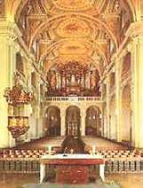 An ornate church interior with high ceilings, chandeliers, and an altar at the center.