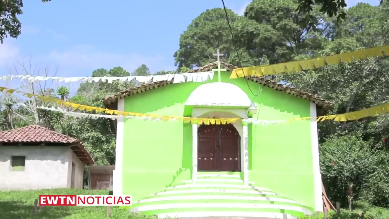 Exterior of the small green chapel in El Espinal where the miracle occurred. The chapel is decorated with festive bunting and topped with a white cross, surrounded by lush tropical vegetation in the highlands of Intibucá.