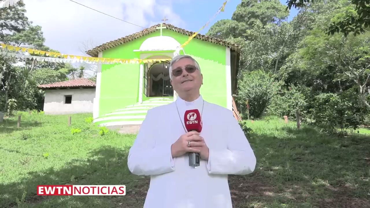 Bishop Walter Guillén Soto, the first bishop of the Diocese of Gracias, standing in front of the El Espinal chapel where the miracle occurred. He wears white episcopal vestments with a pectoral cross and holds an EWTN microphone during the field report in which he recognized the event as a Eucharistic miracle.