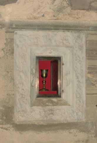 A golden chalice displayed in a red alcove within a stone wall.