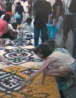 A child creating a colorful floral carpet during a festival, surrounded by people.