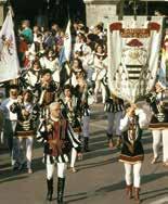 A procession with people in traditional attire carrying banners through a street.