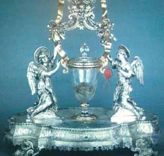 An ornate silver reliquary featuring two angels holding a glass container with blood.