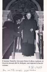 A black and white photo of a priest descending stairs, possibly in a church setting.