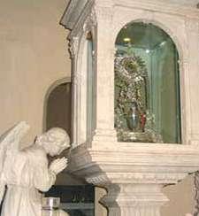 A glass case with a religious relic, featuring an angel in prayer beside it.