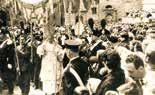 A historical procession with people holding banners and a religious figure in the center.