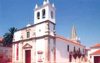 A white church with a bell tower and red-tiled roof under a clear blue sky.