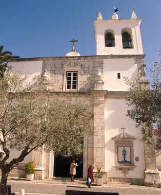 A church facade with a bell tower and cross, surrounded by trees and people entering.