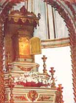 An ornate altar with a golden tabernacle surrounded by flowers and religious symbols.