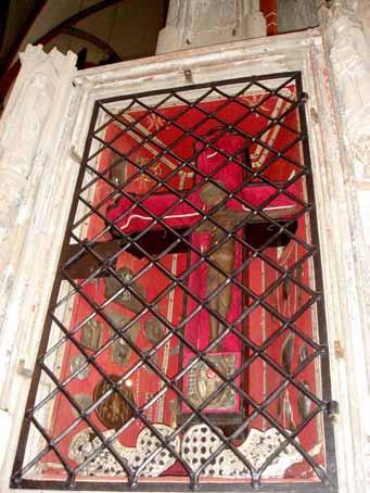 Decorative cross behind black metal grate, symbolizing the 1280 Kranenburg Eucharistic miracle, displayed in a church setting.