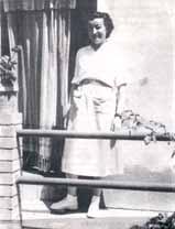 A woman standing on a balcony, smiling, wearing a white dress and shoes.