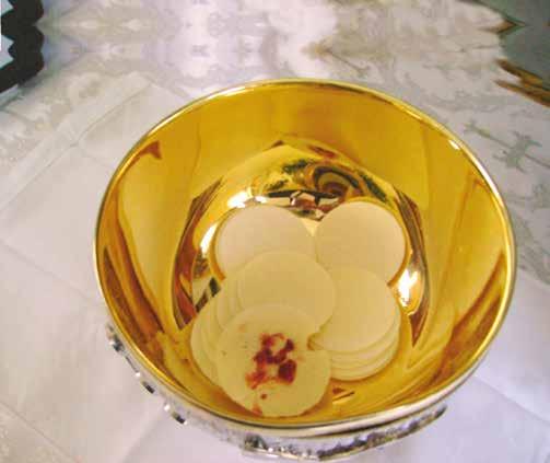 A golden bowl containing Eucharistic hosts with a reddish substance on one of them.