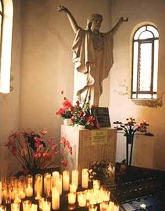 A statue of Jesus with arms outstretched, surrounded by lit candles and floral arrangements.