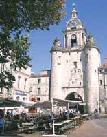 A historic church with a tall tower and archway, surrounded by outdoor seating and trees.