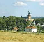 A rural landscape with a church tower rising above trees and fields under a blue sky.