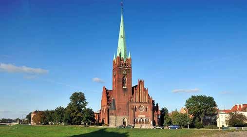 Image of a red brick church with a green spire and surrounding trees.