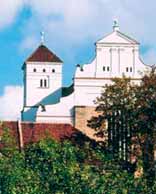 A church building with two towers and a red roof, surrounded by trees.
