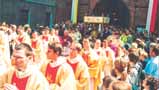 A procession of clergy and people in ceremonial robes walking through a crowd.