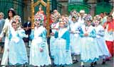 A group of children in white and blue dresses participating in a religious procession.