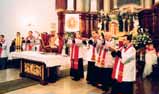 A group of priests in white robes with red stoles conducting a ceremony in a church.