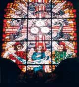 A stained glass window depicting three angels with wings, holding a cloth, surrounded by vibrant colors.
